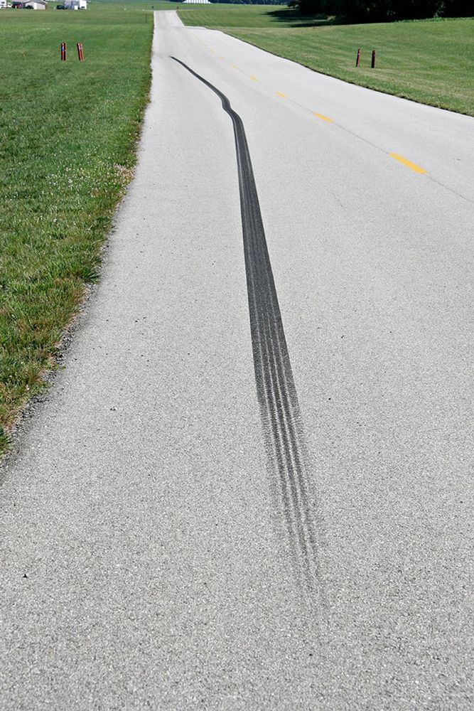 A skid mark on a paved country road stretches well into the distance.