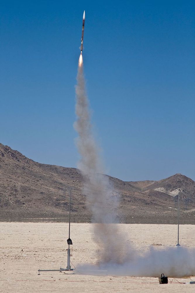 A model rocket launches into the sky in the middle of the desert. 