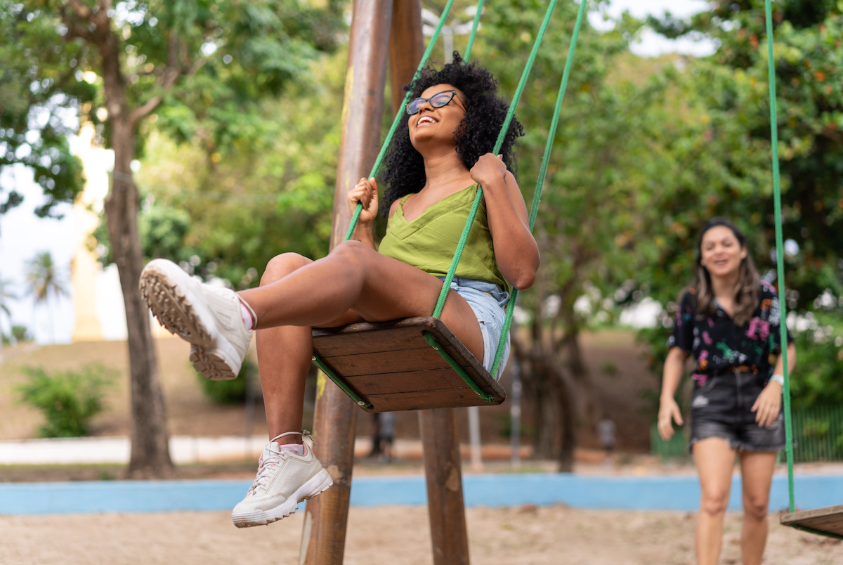 A happy teenager plays on swings while friends look on in a playground
