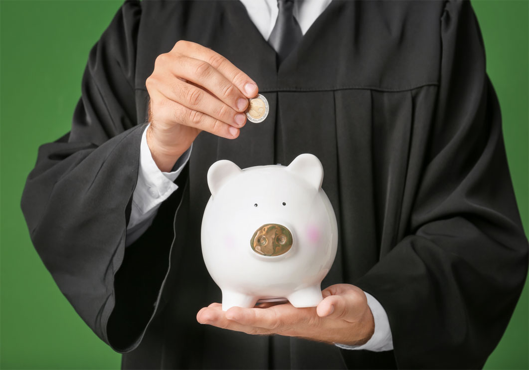 Someone in a graduation outfit is putting coins in a piggy bank.