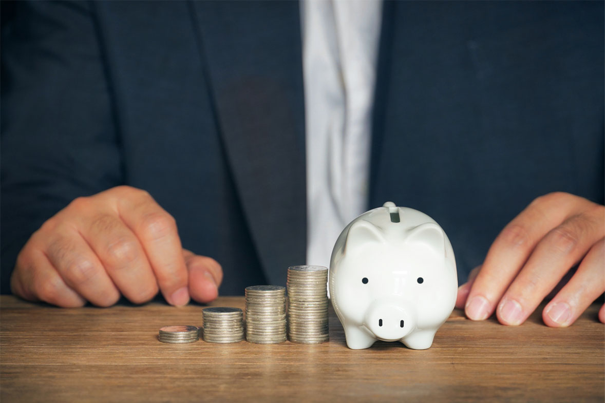 A person sits at a desk displaying a piggy bank wih carefully stacked coins next to it.