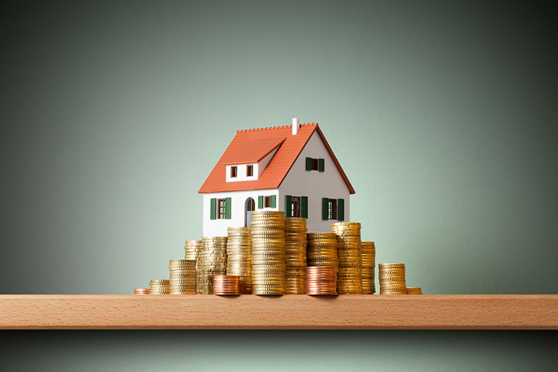 A miniature model home with stacks of coins piling up to the roof.