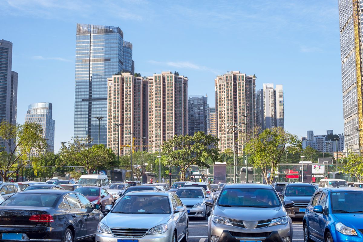 Cars parked in a large parking lot just near a busy urban centre.
